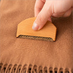 Clothes fabric shaver with light wood handle and dark bristle head removing fabric shaver lint from tan wool sweater