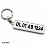 White plastic custom number plate keychain with black embossed text and silver metal ring for car enthusiasts