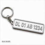Silver metallic custom number plate keychain with raised lettering personalized for car enthusiasts
