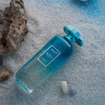 A translucent turquoise glass bottle of next aqua eau de toilette perfume with a metallic cap and minimalist label for korean skin care