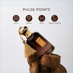 A dark amber glass perfume bottle with a gold cap and tassel labeled arabian scent next for skin care use