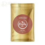 The Beauty Co. De-tan Coffee Face & Body Scrub 100g packaging showing detoxifying and rejuvenating properties for removing tan and restoring skin tone